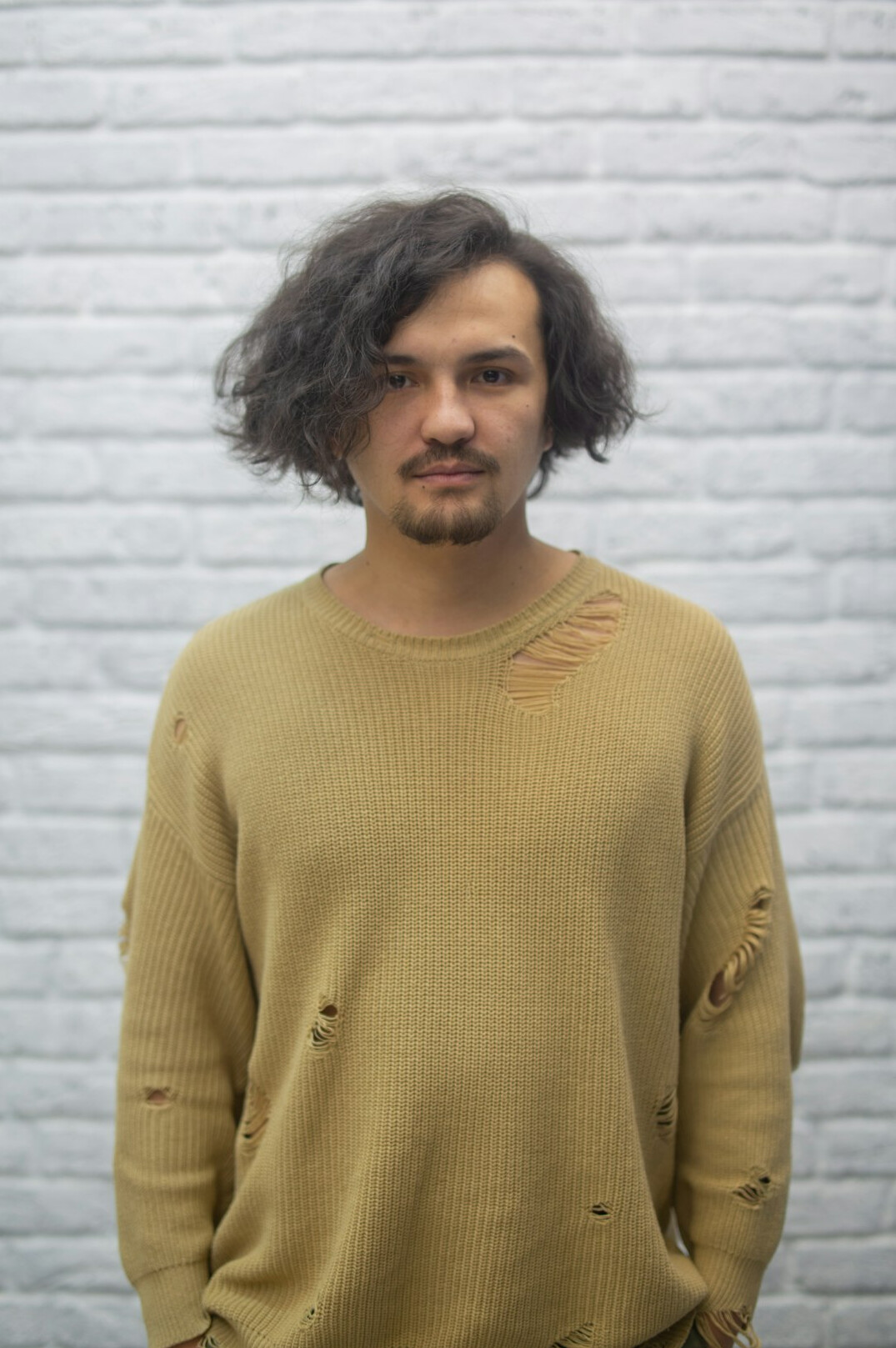 Studio portrait of a white man with short beard and glasses wearing a knit sweater